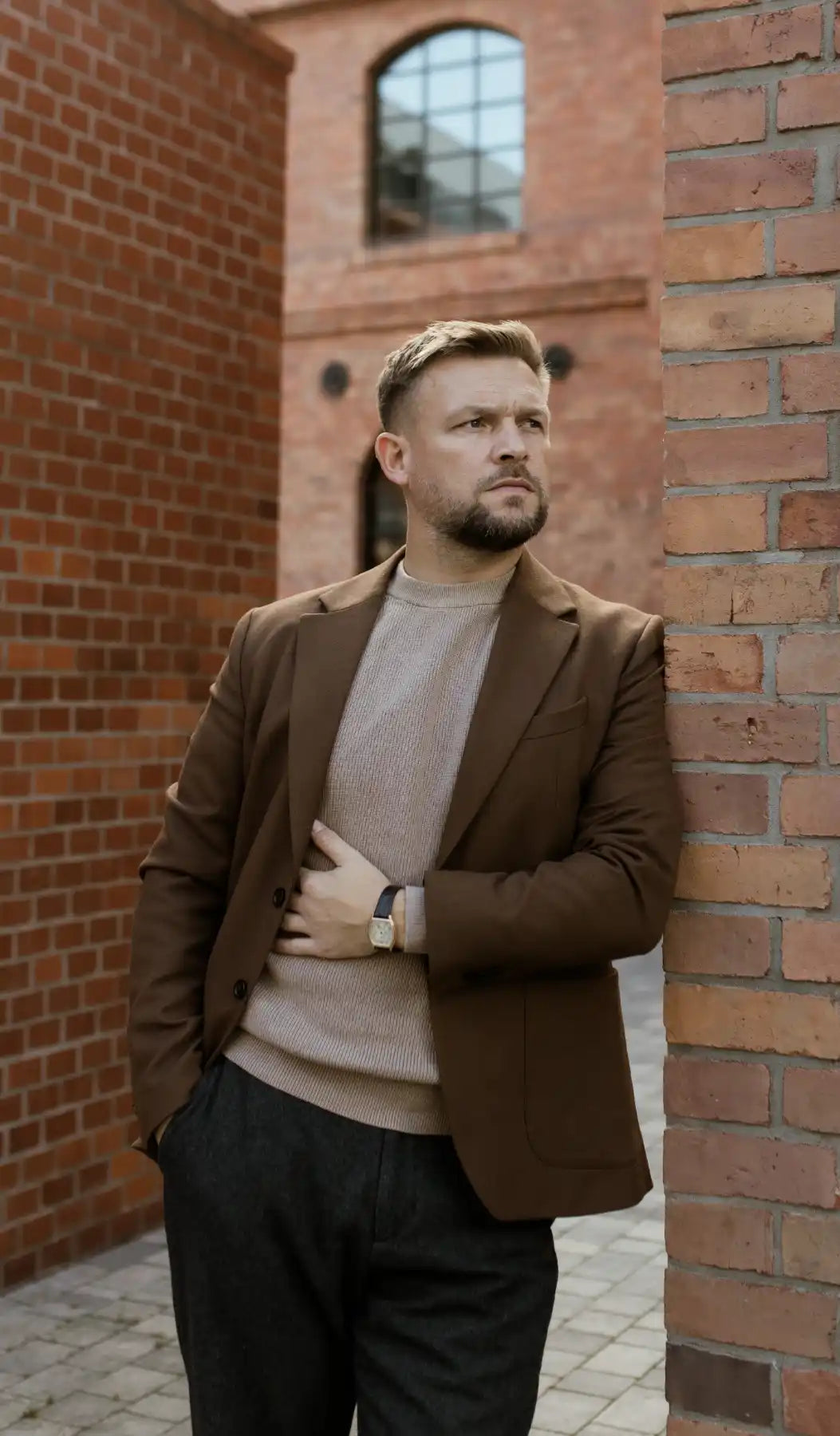 Man in an elegant outfit wearing a luxury wristwatch against a brick building backdrop