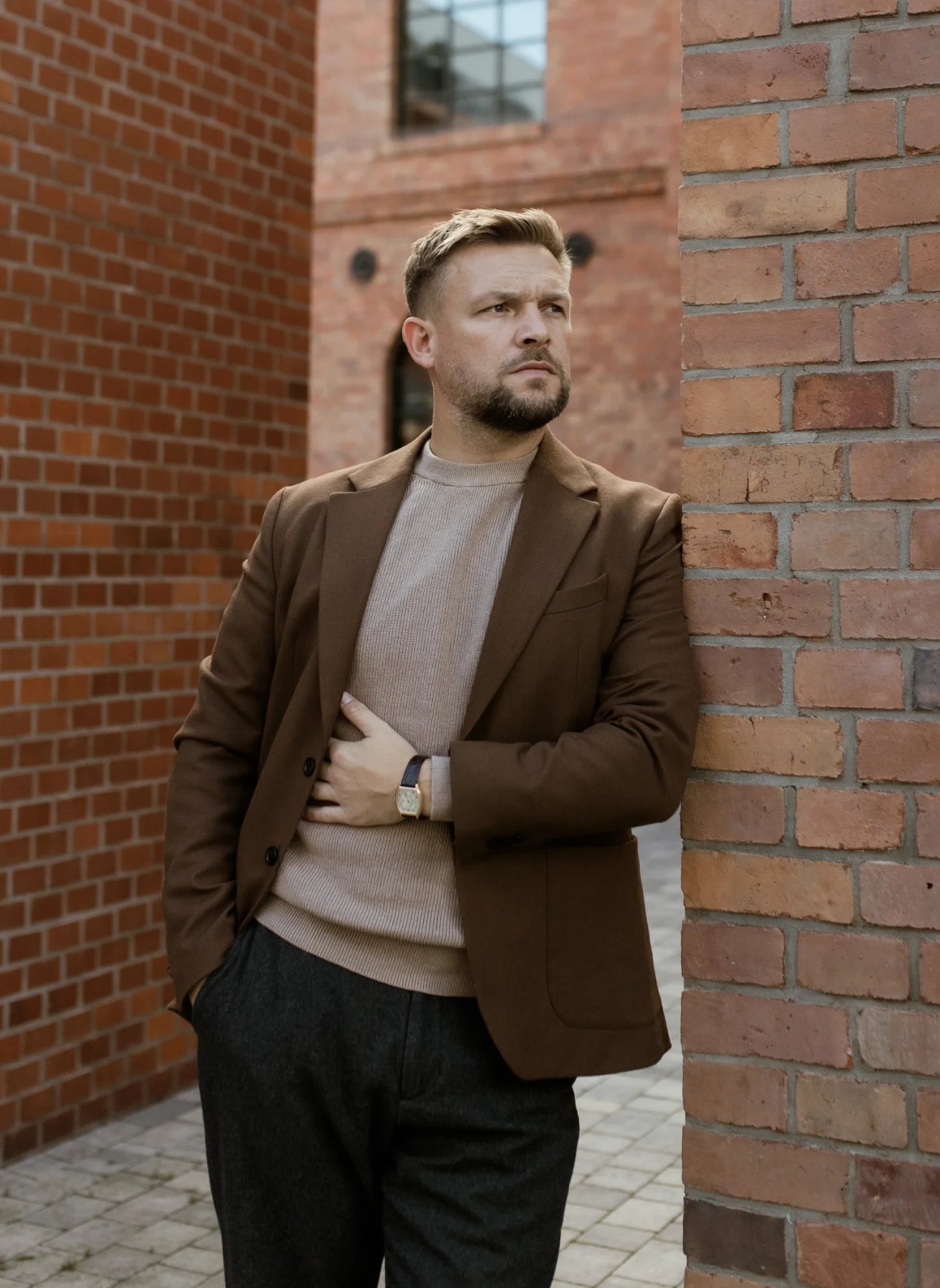 Man in an elegant outfit wearing a luxury wristwatch against a brick building backdrop