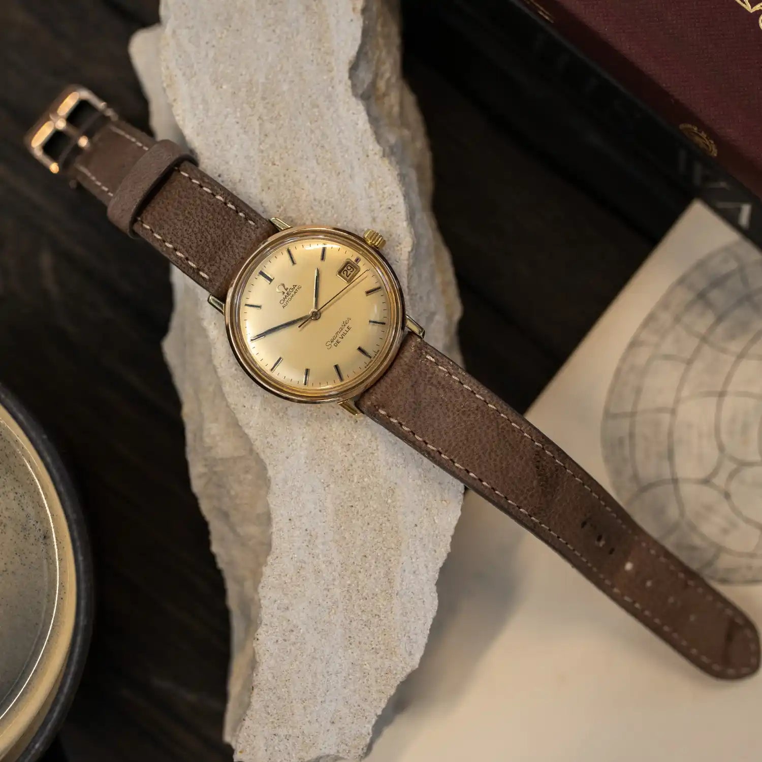 Vintage Omega Seamaster gold-tone wristwatch with cream dial, date window, and brown leather strap
